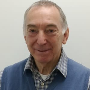 Dr. John Walton, smiling, wearing a blue sweater vest over a plaid shirt